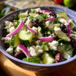 Close-up of a refreshing cucumber feta salad with chunks of cucumber, feta cheese, red onion, olives, and mint.