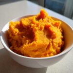 A close-up of vibrant orange, thick Slow Cooker Pumpkin Puree mounded in a white ceramic bowl.