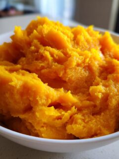 A close-up of bright orange, fluffy Slow Cooker Pumpkin Puree served in a white bowl.