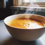 A close-up of a steaming white bowl filled with rich, orange Beer Cheddar Cheese Soup.
