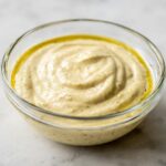 A close-up of creamy Ultimate Caesar Dressing in a glass bowl, with a swirl pattern and a hint of olive oil.
