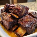 Close-up of tender, glazed Ultimate Smoked Beef Short Ribs in a white dish, glistening with juices.