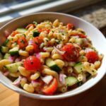 A close-up of a bowl filled with zesty pasta salad, featuring cavatappi pasta, cherry tomatoes, cucumber, and red onion.