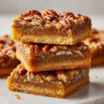 Drie gestapelde Caramel Pecan Pie Bars met een dikke karamelvulling en pecannoten bovenop.