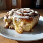 Close-up van een zachte Carrot Cake Cinnamon Roll met romig wit glazuur op een wit bord.