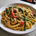 Een close-up van een bord met romige Chicken Pasta Primavera, vol met kip, asperges, paprika en Parmezaanse kaas.