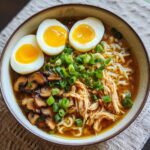 Een kom met heerlijke Chicken Ramen Noodles, gegarneerd met zachtgekookte eieren, gesneden champignons en lente-ui.
