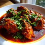 Close-up van een kom met rijke, rode Chicken Rogan Josh, gegarneerd met verse groene koriander.