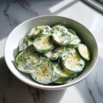 Een kom met plakjes komkommer in een romige dressing, gegarneerd met dille, voor een Creamy Cucumber Salad.
