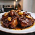 Close-up van glanzende stukken Easy Chicken Adobo, bedekt met een donkere saus en hele knoflooktenen.