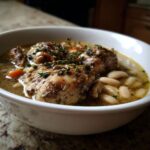 Close-up van een witte kom gevuld met Easy Chicken Cassoulet, met stukken kip, witte bonen en tijm.