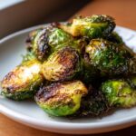 Close-up van knapperige, geroosterde Easy Smashed Brussel Sprouts met peper en zout op een wit bord.