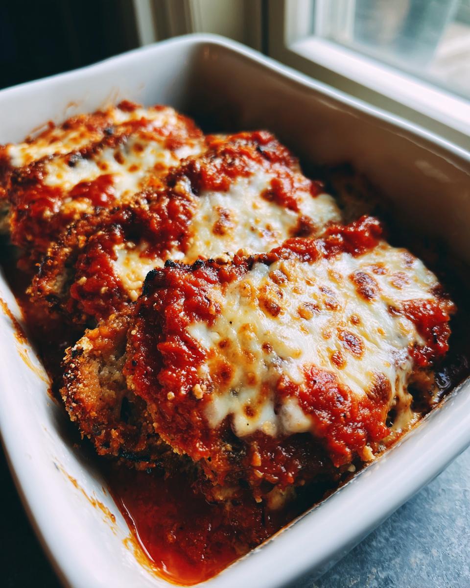 Drie porties Eggplant Parmesan met gesmolten kaas en tomatensaus in een witte ovenschaal.