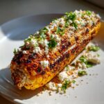 Gegrilde ma&iuml;skolf, bereid als Elote Mexican Street Corn, bedekt met verkruimelde kaas en verse peterselie.