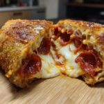 Doorsnede van een Fried Pizza Sandwich met smeltende mozzarella en pepperoni op een houten plank.