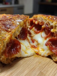Doorsnede van een Fried Pizza Sandwich met smeltende mozzarella en pepperoni op een houten plank.