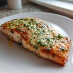 Gegrilde zalmfilet met knoflookboter en peterselie, geserveerd op een wit bord. Heerlijke Garlic Butter Baked Salmon.