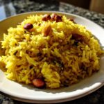 Close-up van een portie felgele Lemon Rice, gegarneerd met geroosterde pinda's, geserveerd op een wit bord.