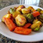 Close-up van geroosterde spruitjes en wortelen, perfect gekarameliseerd, geserveerd op een wit bord.