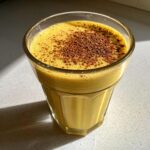 Een glas met romige, gele Homemade Eggnog, gegarneerd met een royale laag cacaopoeder.