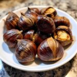 Een stapel glanzende, donkerbruine geroosterde kastanjes, waarvan sommige open zijn om de zachte binnenkant te tonen.