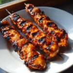 Drie sappige, gegrilde kipspiesjes met een glanzend honingglazuur en donkere grillstrepen op een wit bord.