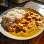 Close-up van een bord met gele Mulligatawny Stew, kipstukjes, wortel en witte rijst.