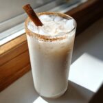 Hoog glas met ijskoude Homemade Horchata, gegarneerd met kaneel op de rand en een stokje.