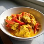 Gedetailleerde close-up van romige Instant Pot Coconut Chicken Curry met stukjes kip en rode paprika in een witte kom.