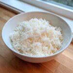 Close-up van een witte kom gevuld met luchtige, witte Instant Pot Jasmine Rijst op een houten aanrecht.