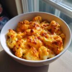 Close-up van een witte kom gevuld met Kaasachtige Gebakken Bloemkool met een goudbruin gegratineerd kaaskorstje.