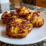 Vier goudbruine, krokante Airfryer Smashed Potatoes op een wit bord, duidelijk de geplette textuur tonend.