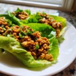 Drie Chicken Lettuce Wraps gevuld met gekruid gehakt en lente-ui op een wit bord.