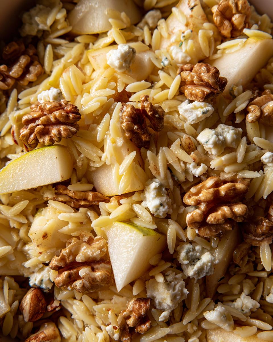 Close-up van een romige Orzo Salade Met Peren Walnoten En Gorgonzola, met stukjes peer en walnoten.