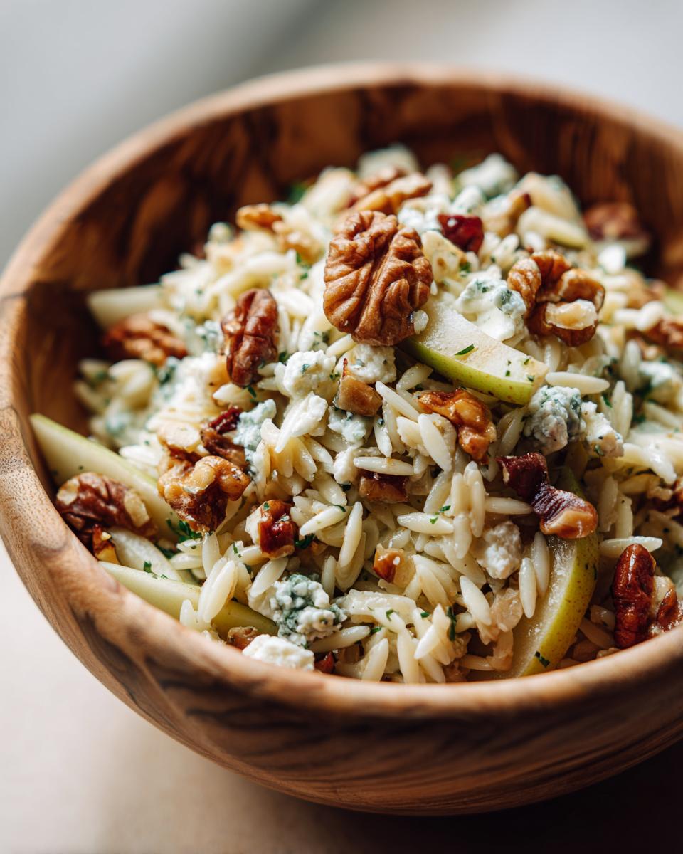 Close-up van een Orzo Salade met Peren Walnoten en Gorgonzola in een rustieke houten kom.
