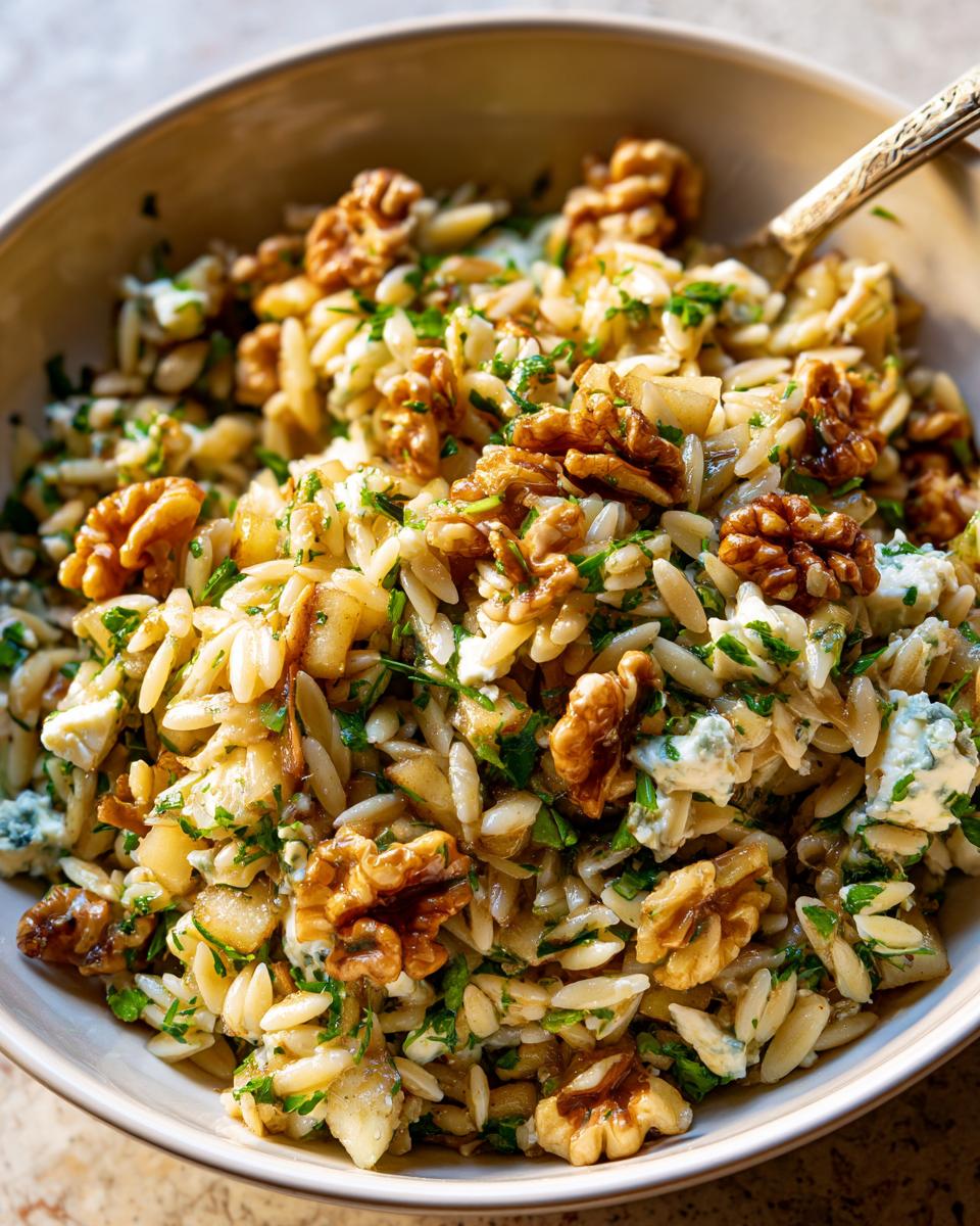 Close-up van een kom Orzo Salade met Peren Walnoten en Gorgonzola, rijkelijk gegarneerd met walnoten.