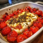 Een blok gebakken feta omringd door geroosterde cherrytomaten, gekruid met kruiden.