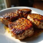 Close-up van vier goudbruin gebakken Pan Seared Pork Medallions op een wit bord met jus.