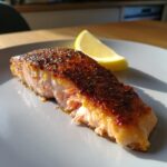 Close-up van een stuk Pan Seared Salmon met een donkere, krokante korst en een partje citroen.