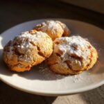Drie goudbruine Peach Cookies rijkelijk bestrooid met poedersuiker op een wit bord.