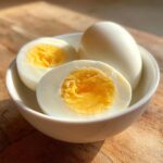 Drie perfect hardgekookte eieren, waarvan twee doormidden gesneden, in een wit kommetje. Dit zijn de Perfect Hard Boiled Eggs.