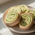 Drie gesneden Pinwheel Sandwiches met een opvallende groene vulling op een licht bord.