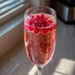 Close-up van een Pomegranate Mimosa in een fl&ucirc;teglas, gevuld met roze bubbels en gegarneerd met rode granaatappelpitjes.