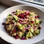 Close-up van een kom met Pomegranate Quinoa Salad, met komkommer, rode ui en granaatappelpitjes.