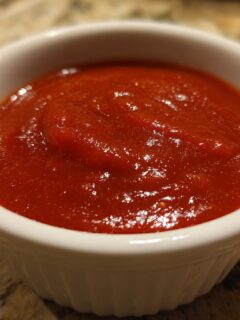 Close-up van helderrode, dikke Enchilada Sauce in een klein wit kommetje op een gespikkeld aanrecht.