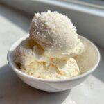 Drie bollen romige, witte Cottage Cheese Ice Cream in een klein wit kommetje, badend in zonlicht.