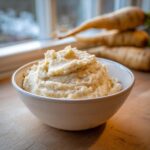 Een kom met romige, gestampte Mashed Turnips (raapjespuree) op een houten tafel, met rapen op de achtergrond.