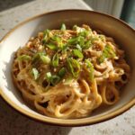 Close-up van romige Peanut Butter Ramen gegarneerd met lente-ui en sesamzaadjes.