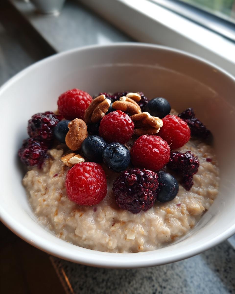 Close-up van romige Protein Oatmeal in een witte kom, getopt met frambozen, blauwe bessen, bramen en pecannoten.