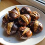 Geroosterde kastanjes met zout en peper, opengebarsten op een wit bord.